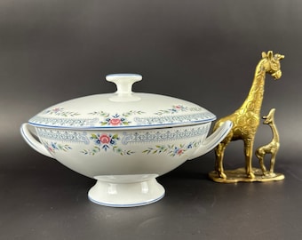 Può includere: Una zuppiera di servizio in porcellana bianca con coperchio, con un design blu e floreale. La zuppiera ha due manici e una base a piedistallo.