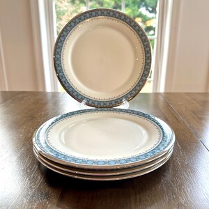 May include: A set of four white ceramic dinner plates with a blue and gold floral border.
