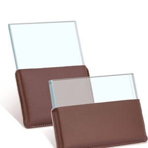May include: Two glass magnifiers with brown leather cases. The magnifiers are rectangular and have a clear glass surface. The cases are made of brown leather and have a stitched edge.