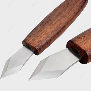 May include: Two wood handled carving tools with a pointed blade. The tools are made of metal and have a brown wooden handle.
