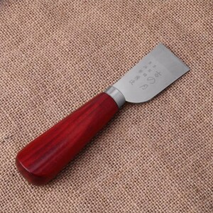 Puede incluir: Un cuchillo para trabajar el cuero con un mango de madera pulida de color marr&oacute;n rojizo y una hoja plateada. La hoja tiene caracteres japoneses grabados. El cuchillo est&aacute; dise&ntilde;ado para cortar y dar forma al cuero con precisi&oacute;n.