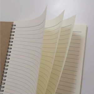 May include: A spiral bound notebook with a brown paper cover and lined pages. The pages are cream coloured and have a subtle texture.