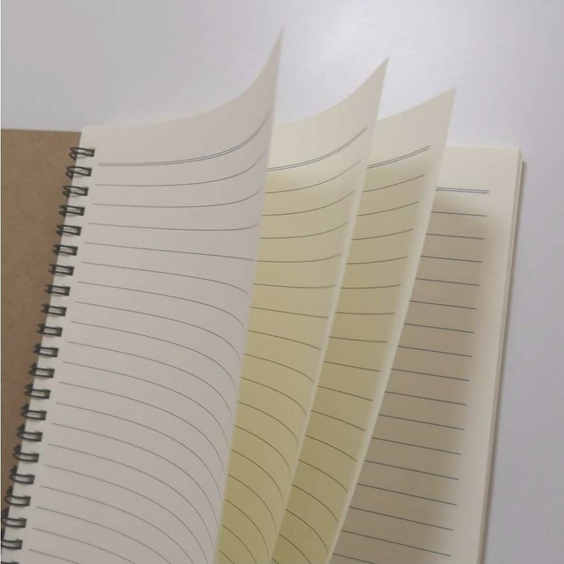 May include: A spiral bound notebook with a brown paper cover and lined pages. The pages are cream coloured and have a subtle texture.