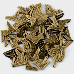 May include: A collection of numerous L-shaped metal corner protectors featuring an antique brass finish and embossed scrollwork patterns. Each piece is designed with two perpendicular sides and small circular holes for attachment to edges.