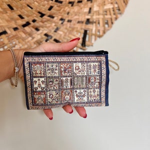 May include: A small, blue zippered pouch with a colorful patterned fabric design. The pouch has a gold chain attached to the zipper.