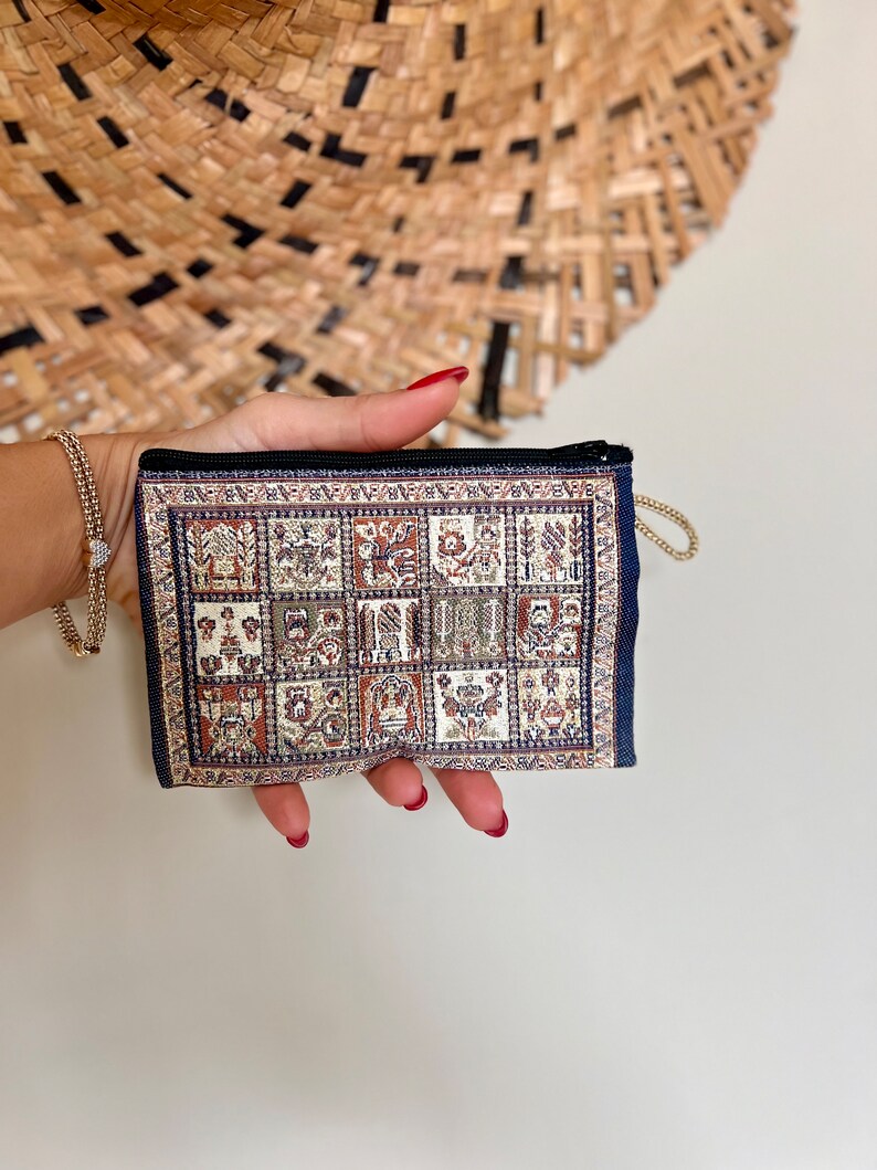 May include: A small, blue zippered pouch with a colorful patterned fabric design. The pouch has a gold chain attached to the zipper.