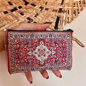 May include: A small red zippered pouch with a colorful patterned design resembling a rug. The pouch has a gold zipper and a gold tassel.