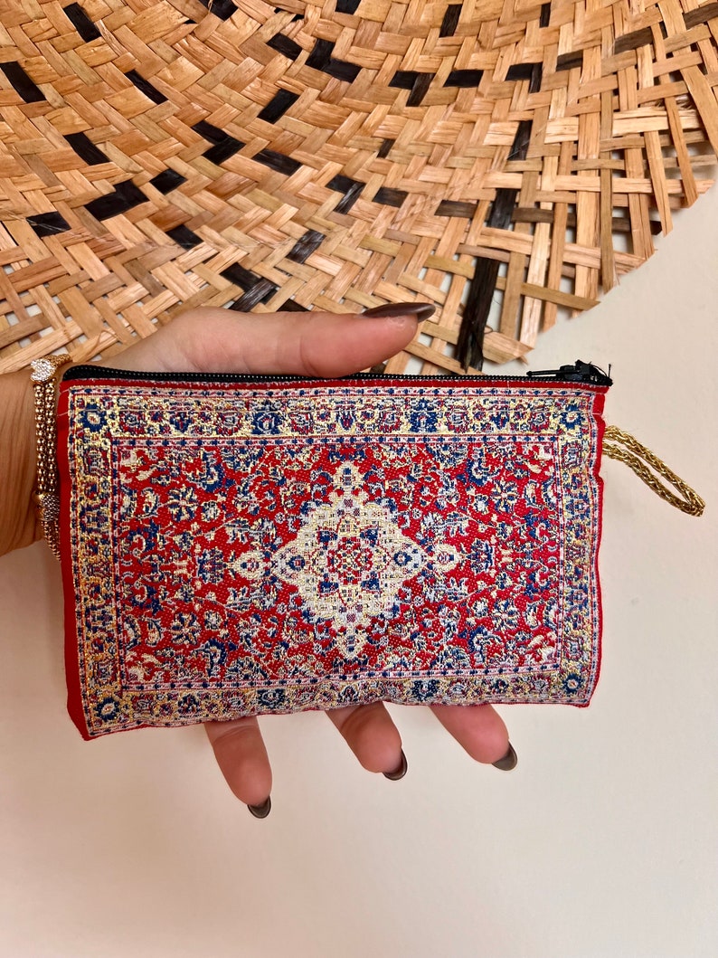 May include: A small red zippered pouch with a colorful patterned design resembling a rug. The pouch has a gold zipper and a gold tassel.