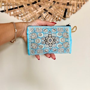 May include: A small blue pouch with a gold and black patterned design. The pouch has a zipper closure and a gold tassel.