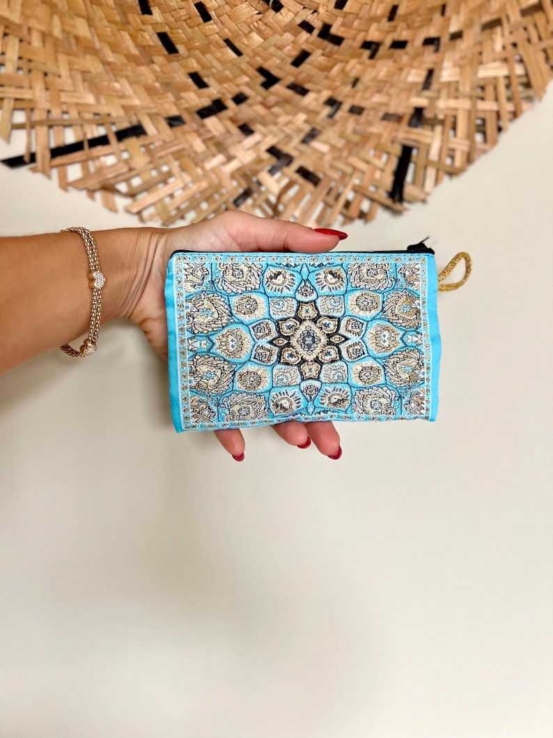 May include: A small blue pouch with a gold and black patterned design. The pouch has a zipper closure and a gold tassel.