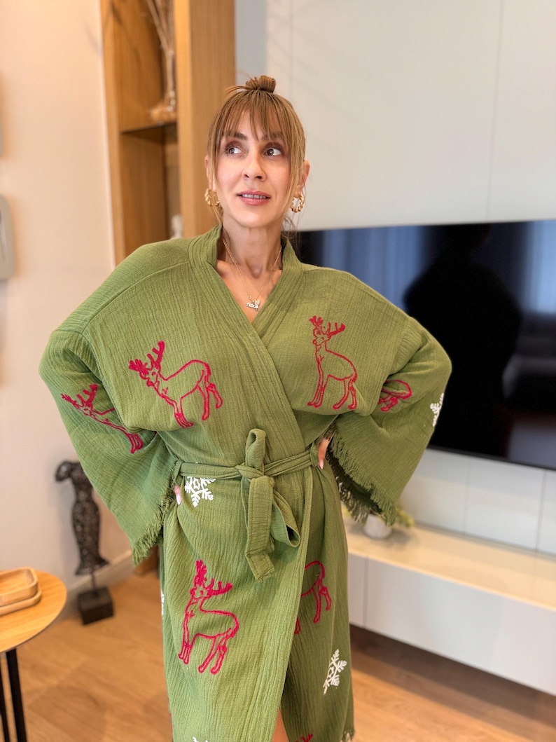 K&ouml;nnte beinhalten: Eine gr&uuml;ne Robe mit einem roten Rentiermuster und wei&szlig;en Schneeflocken-Akzenten. Die Robe hat einen Bindeg&uuml;rtel und Fransenbesatz.