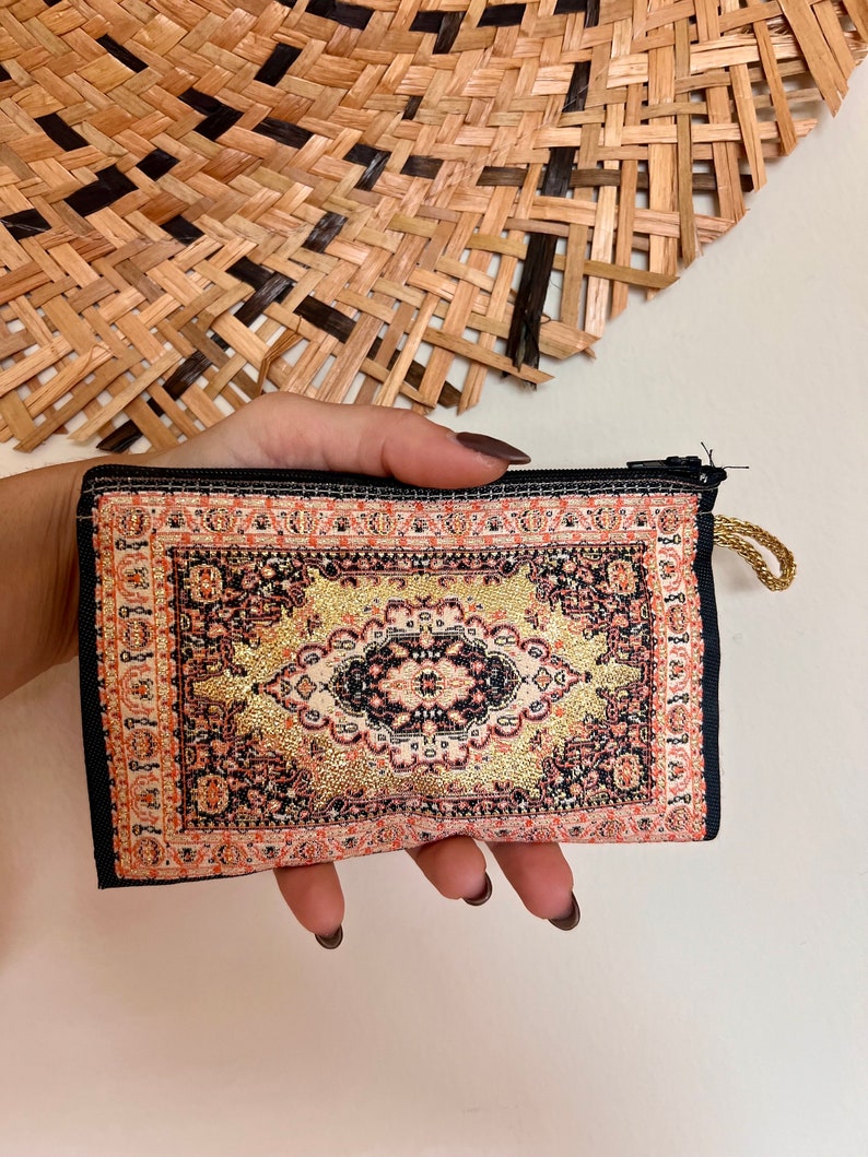 May include: A small black zippered pouch with a colorful rug design. The rug design features a central diamond shape with gold accents.