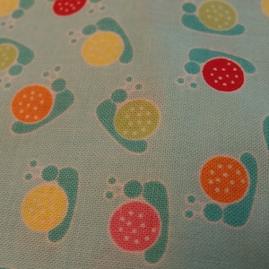 May include: A turquoise fabric with a repeating pattern of footprints. Each footprint has a different colored circle in the center, including red, orange, yellow, green, and pink.