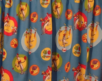 May include: Blue fabric with a repeating pattern of a cat wearing a red and white hat juggling various fruits and vegetables. The background is a light blue with yellow, green, and red circles.