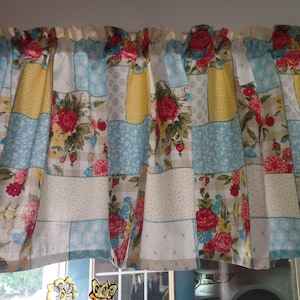 May include: A patchwork valance with a floral pattern in shades of red, yellow, blue, and white. The valance has a ruffled edge and is made of a soft, cotton fabric.
