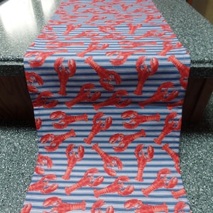 May include: A blue and white striped table runner with a red lobster pattern.