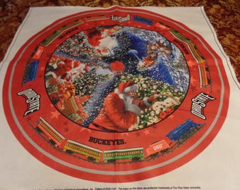 May include: A round, white fabric with a red border featuring a Christmas scene with Santa Claus, gifts, and a train. The words "Ohio State" and "Buckeyes" are printed on the fabric.