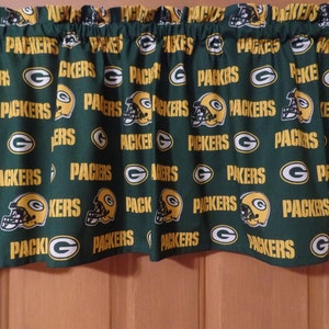 May include: Green and gold fabric valance with a repeating pattern of the Green Bay Packers logo. The logo features a football helmet with a 'G' on the side and the words 'Packers' underneath.