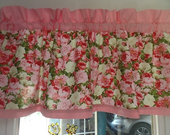 May include: A pink and white floral valance with a ruffled top and bottom edge. The valance is made of a cotton fabric with a floral print. The valance is hung on a window.