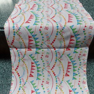 May include: White table runner with a repeating pattern of colorful flags and the words "Hip Hooray Party Time" in a red, blue, green, and yellow font.
