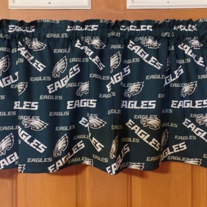 May include: Dark green valance with a repeating pattern of the word "EAGLES" in white, along with the team's logo. The valance is made of fabric and has a ruffled top edge. The valance is designed to be hung above a window.