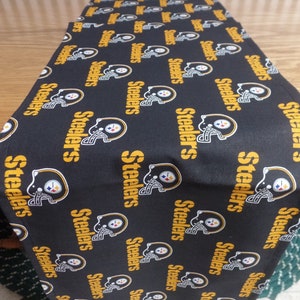 May include: Black and gold table runner with the repeated word "Steelers" printed on it.