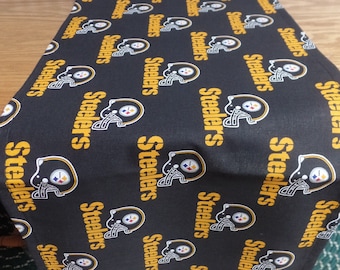 May include: Black and gold table runner with the repeated word "Steelers" printed on it.
