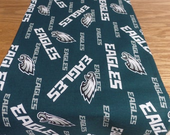 May include: A dark green table runner featuring the word "EAGLES" in white, along with the team's logo. The text and logo are repeated across the fabric. The runner is likely made of a soft material and is suitable for a dining table.