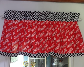 May include: A red window valance featuring the Coca-Cola logo in white script. The valance has a black and white checkered pattern at the top and bottom edges. The valance is hanging on a white rod.