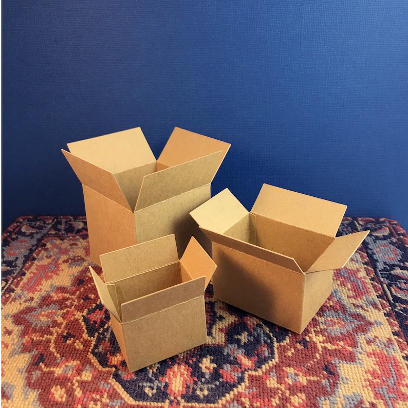 May include: Three open, brown cardboard boxes of varying sizes are arranged on a patterned rug against a blue backdrop. The boxes are empty, with their flaps folded open, suggesting they are ready for use. The boxes are made of corrugated cardboard.