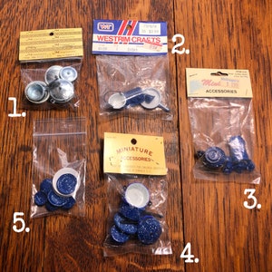 Op de afbeelding: Vijf zakjes met miniatuur keukenaccessoires, waaronder een set blauwe en witte geëmailleerde potten en pannen, een set blauwe en witte geëmailleerde borden, een set zilveren potten en pannen en een set blauwe en witte geëmailleerde kookgerei. De zakjes zijn gelabeld met de merknaam "Miniature Accessories" en de prijs.