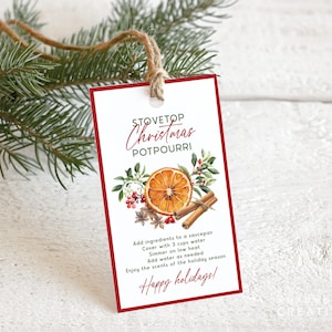 May include: A rectangular tag with a red border and the words "Stovetop Christmas Potpourri" in elegant script. The tag features a watercolor illustration of an orange slice, cinnamon sticks, and spices. The tag is tied with twine and adorned with evergreen branches.