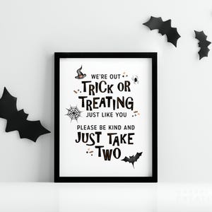 May include: A framed Halloween sign with black text that reads "We're out trick or treating just like you, please be kind and just take two." Black bat cutouts decorate the white wall.