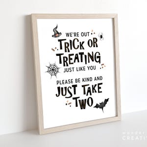May include: A framed Halloween-themed print with the text "WE'RE OUT TRICK OR TREATING JUST LIKE YOU PLEASE BE KIND AND JUST TAKE TWO." The print features a witch's hat, spider, spiderweb, and bat illustrations in black and gold.