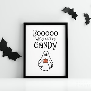 May include: A framed Halloween-themed print with a black frame. The print features the text "Booooo We're Out of Candy" above a cartoon ghost holding a pumpkin. Black bat cutouts decorate the white wall.