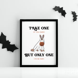 May include: A framed Halloween-themed print with a black frame. The print features a cartoon dog dressed as a ghost, holding a jack-o'-lantern. Text on the print reads "TAKE ONE (IF YOU DARE) BUT ONLY ONE (TO BE FAIR)". Black bat cutouts decorate the wall.