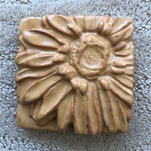 Peut inclure: Un carreau de céramique avec un motif en relief de tournesol dans des tons de brun et de beige.