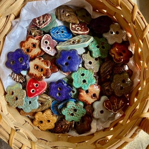 May include: A wicker basket filled with colorful ceramic buttons in various shapes, including flowers, leaves, and hearts. The buttons have a rustic, handmade look and are perfect for adding a touch of whimsy to any project.