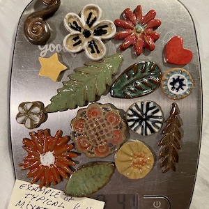 May include: A collection of ceramic decorative pieces in various shapes, including flowers, leaves, and a heart, displayed on a digital scale. The pieces are in shades of red, green, yellow, and white. The scale reads 4.1 lb. Text on a label reads "Example of Typical Mixed Selection".