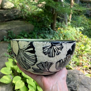 May include: A white ceramic bowl with a black and white ginkgo leaf design. The bowl is hand-crafted and has a unique, textured surface.