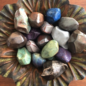 May include: A collection of small, colorful, glazed ceramic rocks in a decorative, brown, leaf-shaped dish.