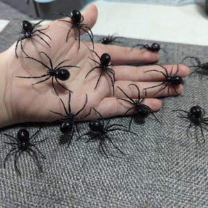 May include: A hand holding a collection of black plastic spiders. The spiders have eight legs and are arranged in a variety of positions.