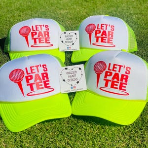 May include: Four golf trucker hats with white fronts and neon green brims and mesh backs. Each hat features the text "LET'S PAR TEE" in red with a golf ball and tee graphic. Small cards with the text "RUGGED HEART DESIGNS" are also present.