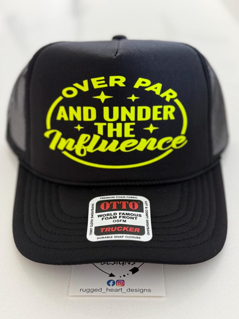 May include: Black trucker hat with a yellow graphic that reads "OVER PAR AND UNDER THE Influence". The hat has a mesh back and a curved brim. A tag on the front reads "OTTO WORLD FAMOUS FOAM FRONT TRUCKER".