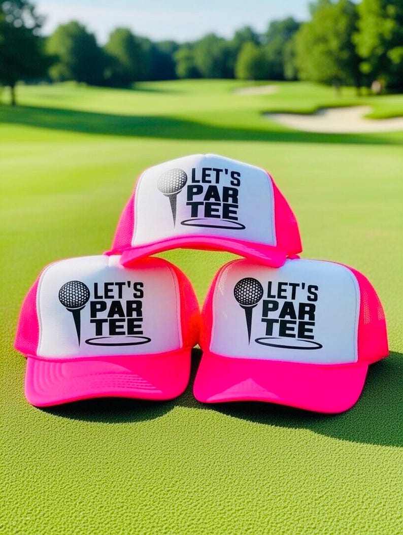 May include: Three neon pink and white trucker hats with the text "LET'S PAR TEE" and a golf ball graphic. The hats are displayed on a green golf course.
