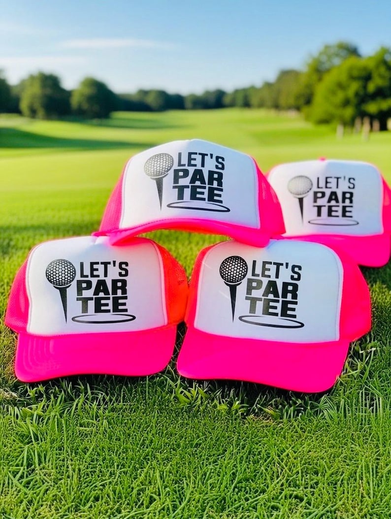 May include: A collection of neon pink and white trucker hats with the text "LET'S PAR TEE" and a golf ball graphic. The hats are displayed on a green grassy field, with a golf course in the background.