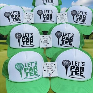 May include: A collection of green and white trucker hats. Each hat features the text "LET'S PAR TEE" with a golf ball and tee graphic. Small cards with the text "RUGGED HEART DESIGNS" are also present.