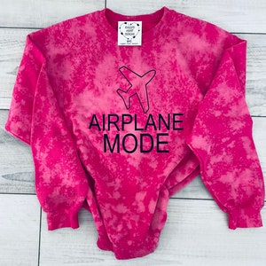 May include: Pink tie-dye sweatshirt with a black airplane graphic and the text "AIRPLANE MODE".