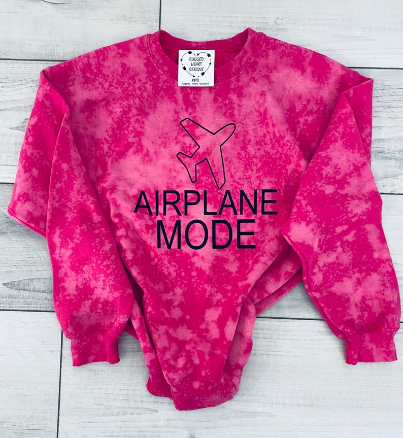May include: Pink tie-dye sweatshirt with a black airplane graphic and the text "AIRPLANE MODE".