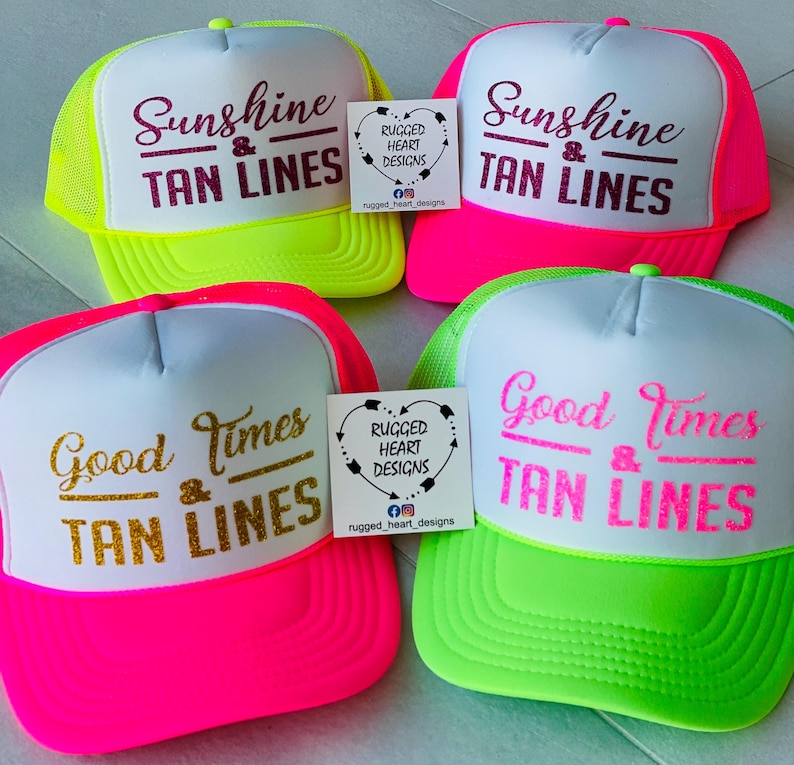 Puede incluir: Cuatro gorras de camionero con paneles frontales blancos y malla trasera de color ne&oacute;n. Dos gorras tienen el texto Sunshine & TAN LINES en granate brillante. Una tiene Good Times & TAN LINES en purpurina dorada y otra en rosa ne&oacute;n.